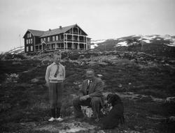 En gutt står og en mann og en hund sitter på bakken med Grot