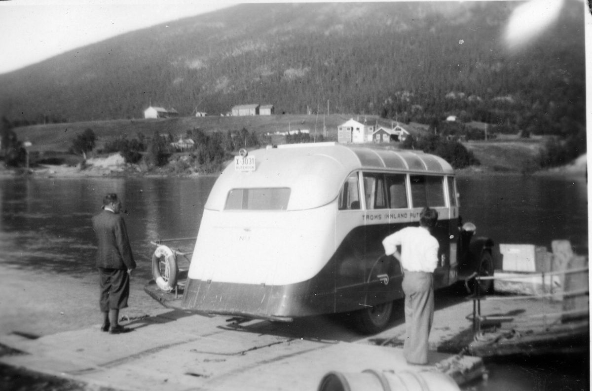En liten rutebuss som trekkes over en elv på en fergepram.  Ved Fredriksberg. Ferje over Målselva. Det gikk ferje to steder, en nede ved Gullhav, den andre sør for Moen. X-3031 står i Norges Bilbok 1935 som en Federal 1930 på Troms Innland Rutebil.  Bilferge.