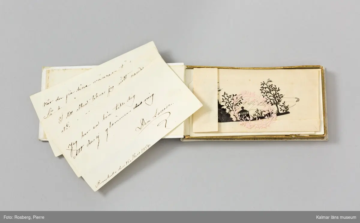 KLM45239:3:2 Poesialbum. En ask i kraftig vit papp med dekor i guld. Sirligt mönster med bland annat rosor i blått, rosa och lila på locket. I asken förvaras samlingar med små papperslappar på vilka vänner skrivit små tänkeord eller hälsningar. Här finns också teckningar (någon signerad Sophie Sundberg) och några mycket fina siluettklipp. Samtliga är signerade och flertalet är daterade någon gång på 1850-talet. På flera står också Rumskulla. I album :3:2 finns 11 stycken blad signerade ”din Louise”, ”din vän Pamela”, Laura Enqvist, Elsie Enqvist, Lina Sundberg, Jenny Ljungberg, Mathilda Nissvandt, Sophia Goldkuhl. :3:2:4 omfattar också två siluettklipp det ena i rosa papper föreställande krans med blommor och blad samt det andra i svart papper som föreställer en miljö med lusthus, träd, klippa, och svan. :5 omfattar också siluettklipp i svart papper föreställande vas med blommor. :6 omfattar också siluettklipp i grönt papper, blommor och blad i form av ett hjärta och i guldpapper ett ymnighetshorn med blommor och blad. :7 är en liten färglagd teckning av en blombukett med bland annat en vit ros samt fyra siluettklipp. Två av svart papper svan och träd samt två damer och en herre som verkar dricka te, en av guldpapper som föreställer ett fantasiföremål med lövverk och blommor, samt en av silverpapper som föreställer blommor och blad. :10 är en blyertsteckning av en fjäril signera Din mamma ( med vilket borde avses Nanny ljungberg). :11 blyertsteckning av tulpan och liljekonvalj signerad Sophie Sundberg den 13 maj 18?