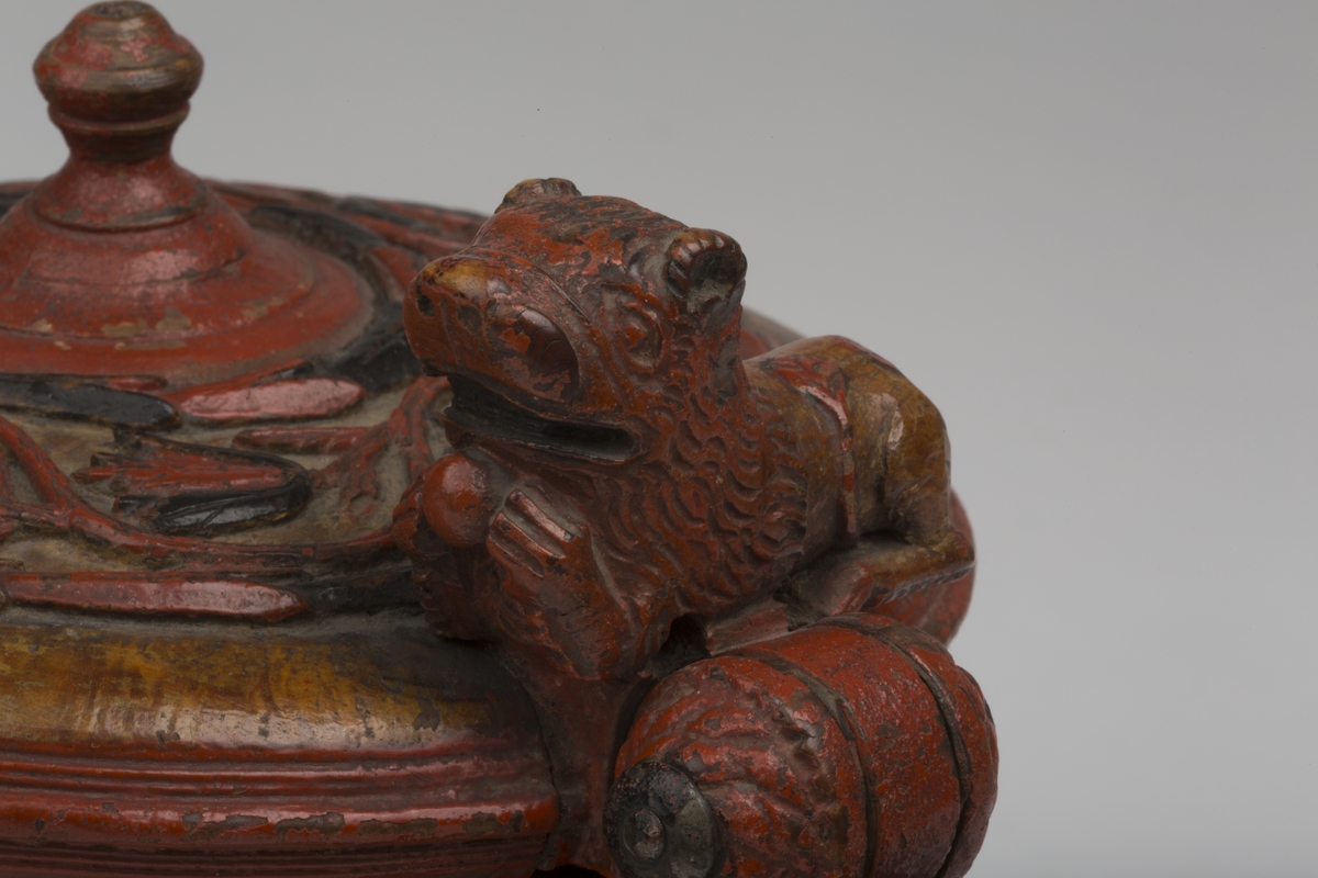 Dekorert med fortløpende billedfrise med dyr og trær på nederste del av korpus. Kannen har løveføtter og løvegjekk og bakkantine som håndtak. 