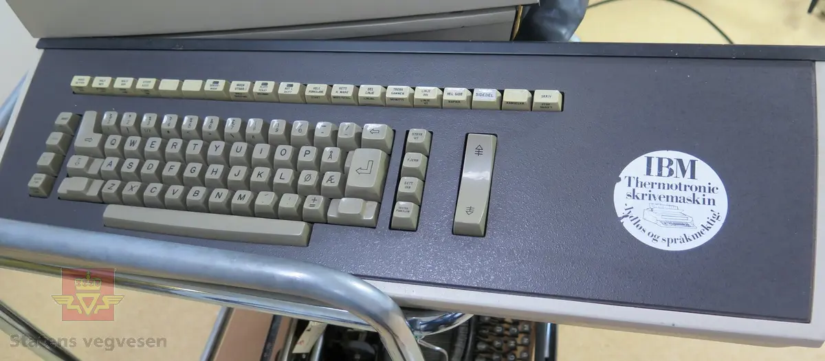 Datamaskin, der skjerm og tastatur henger sammen. I hovedsak hvit og grå/svart. Merking fra produsenten.