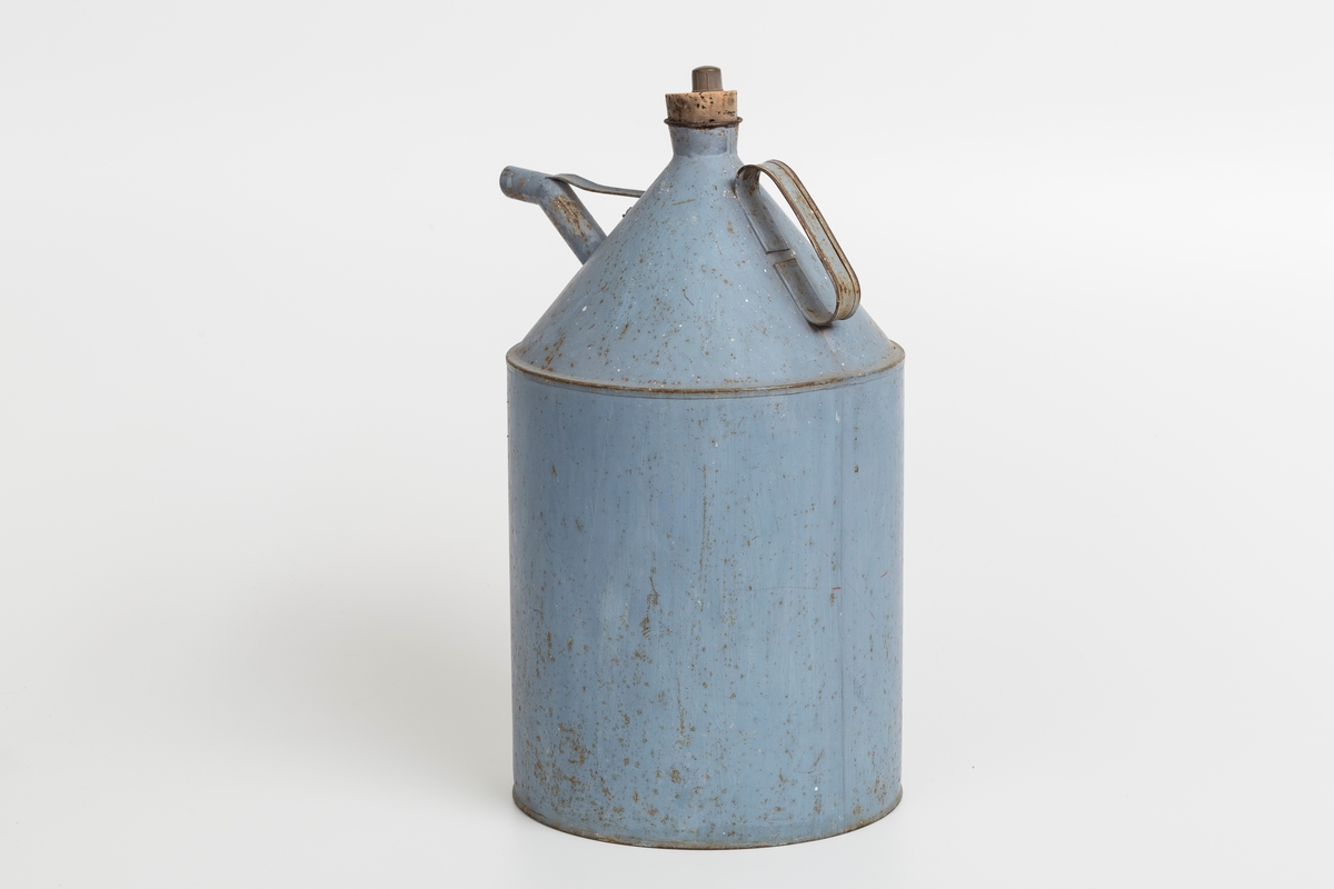 Kanne i sink, blå. Korket i tuten og korklokk med plast. Har håndtak og helletut. Kannen har påklistret god jul merkelapp med navn. Delvis avrevet.