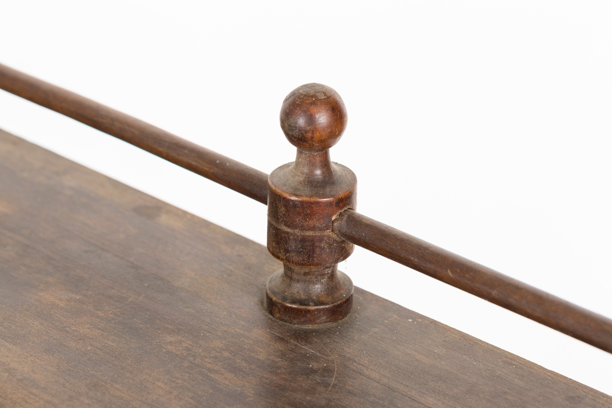 Hylle med 4 hyller. Dreide stolper mellom hyllene. Mangler ett bein. Sprosser øverst. Lakkert i mørk brunt.