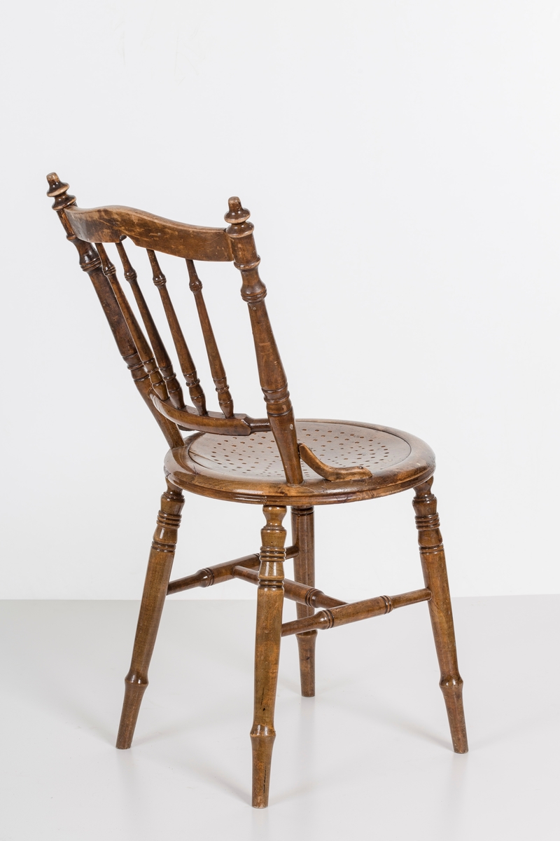 Stol i lakket treverk. Rundt stolsete med hullemønster. Rygg som er svakt buet med spiler og mønster. Dreide ben og spiler i rygg.