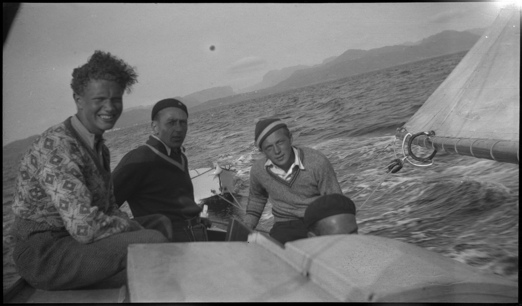 Harald Bergsaker, Ottar Roaldsøy, L. Fosse og Lindtner på den søndre enden av øya Hidle, øst for Stavanger. De er på kanten av et stup og hviler i gresset under stupet. En av dem ser utover sjøen med kikkert. Seilbåten "Vilja ligger i bakgrunnen.