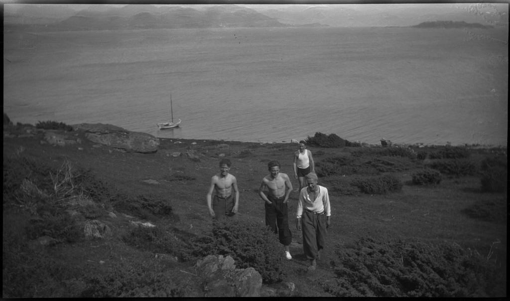 Harald Bergsaker, Ottar Roaldsøy, L. Fosse og Lindtner på den søndre enden av øya Hidle, øst for Stavanger. De er på kanten av et stup og hviler i gresset under stupet. En av dem ser utover sjøen med kikkert. Seilbåten "Vilja ligger i bakgrunnen.