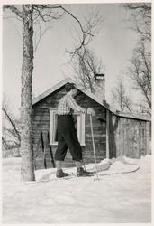 Mann på ski. Hytte i bakgrunnen.