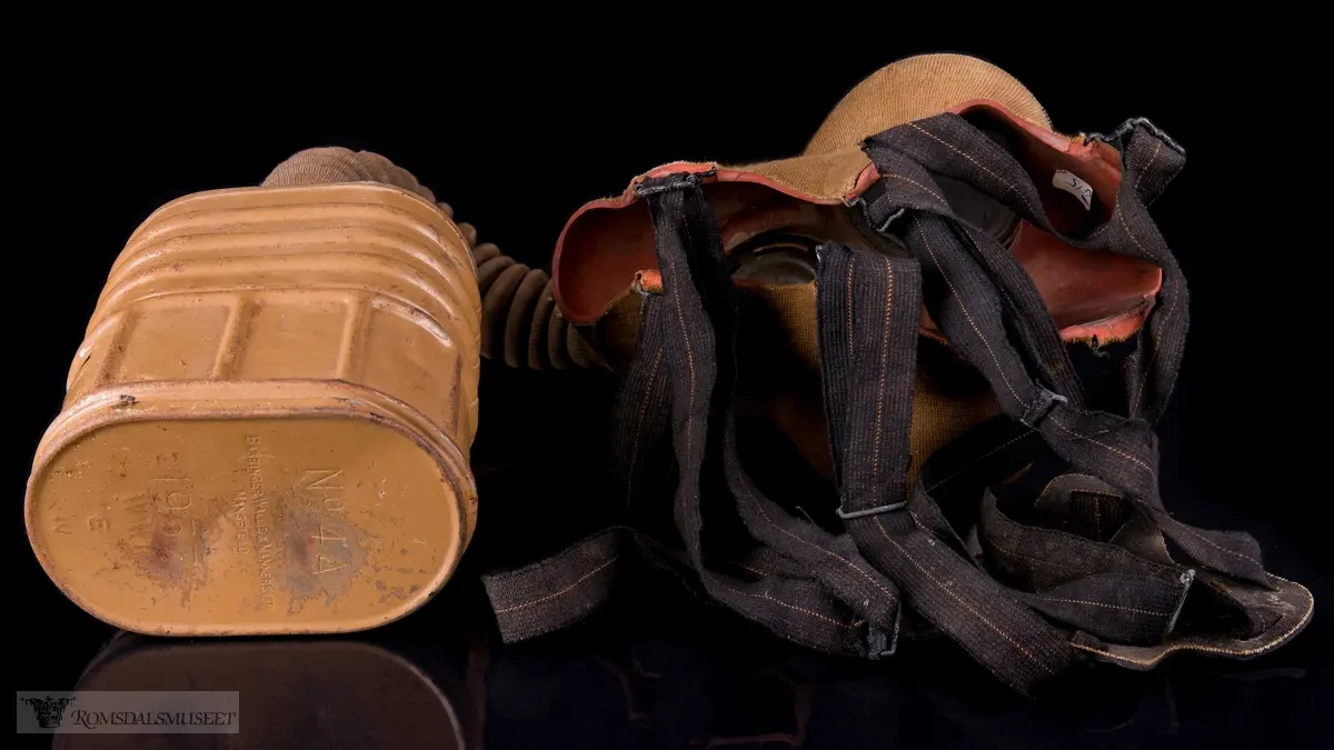 Britisk gassmaske brukt under andre verdenskrig. Ansiktsstykket består av tekstilbelagt gummi. En bøyelig slange går fra den runde, perforerte utlbåsningsventilen til et ovalt, tønneformet filter. Festestropper i gummi med bakhodestykke av lær.