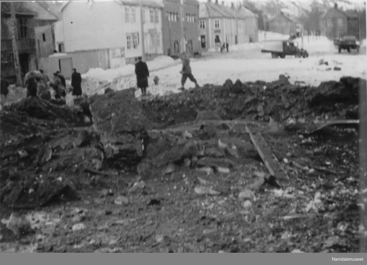 Namsos, 20.04.1940. En av de første bombene har falt ved jernbanestasjonen (C. Gulbrandsons gt.). Folk rømmer unna.
