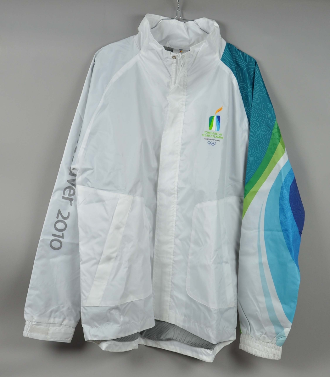 Hvit jakke med flerfarget erme. Motiv av de olympiske ringene laminert på ryggen. Logo for fakkelstafetten i forbindelse med de olympiske vinterleker i Vancouver 2010 er laminert på brystet.