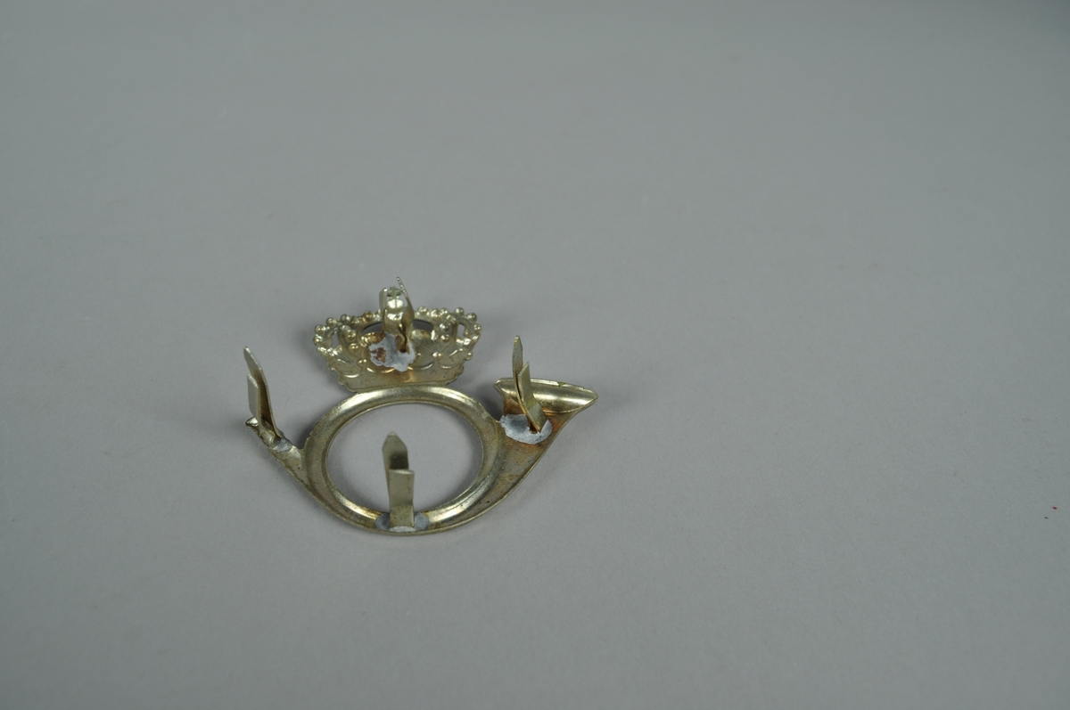 Posthornmerke i sølvfarget metall.