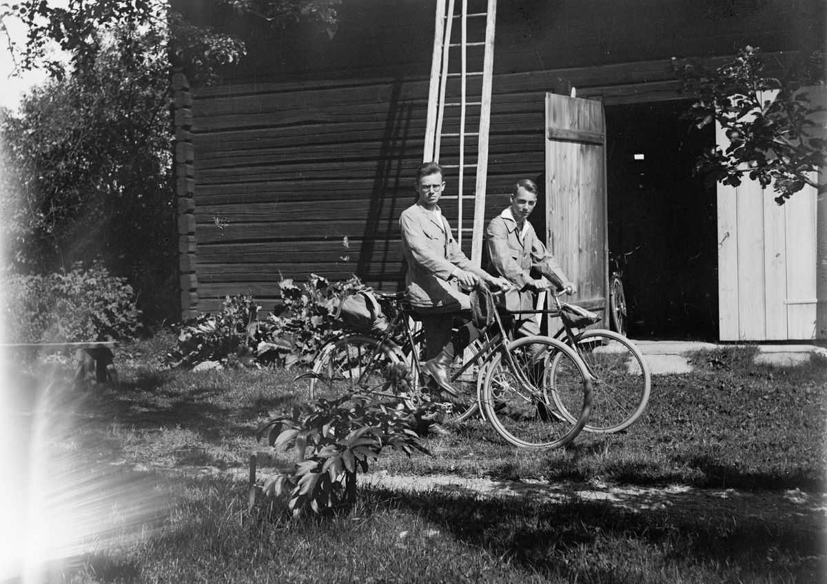 Sannolikt Alf och Ingemar Liljefors med cyklar framför ekonomibyggnad, sannolikt i Sverige