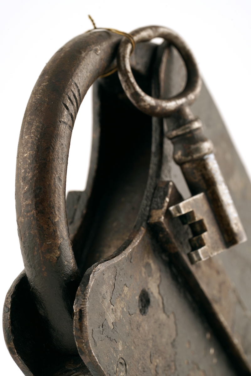 Hengelås av jern. Firkantet med svingbart, rektangulært lokk.
Nøkkel av jern. Oval ring, firkantet skjegg og hul pipe.