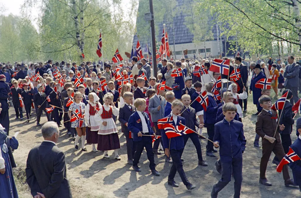 17. mai-tog med barn i penklær og flagg i hendene.