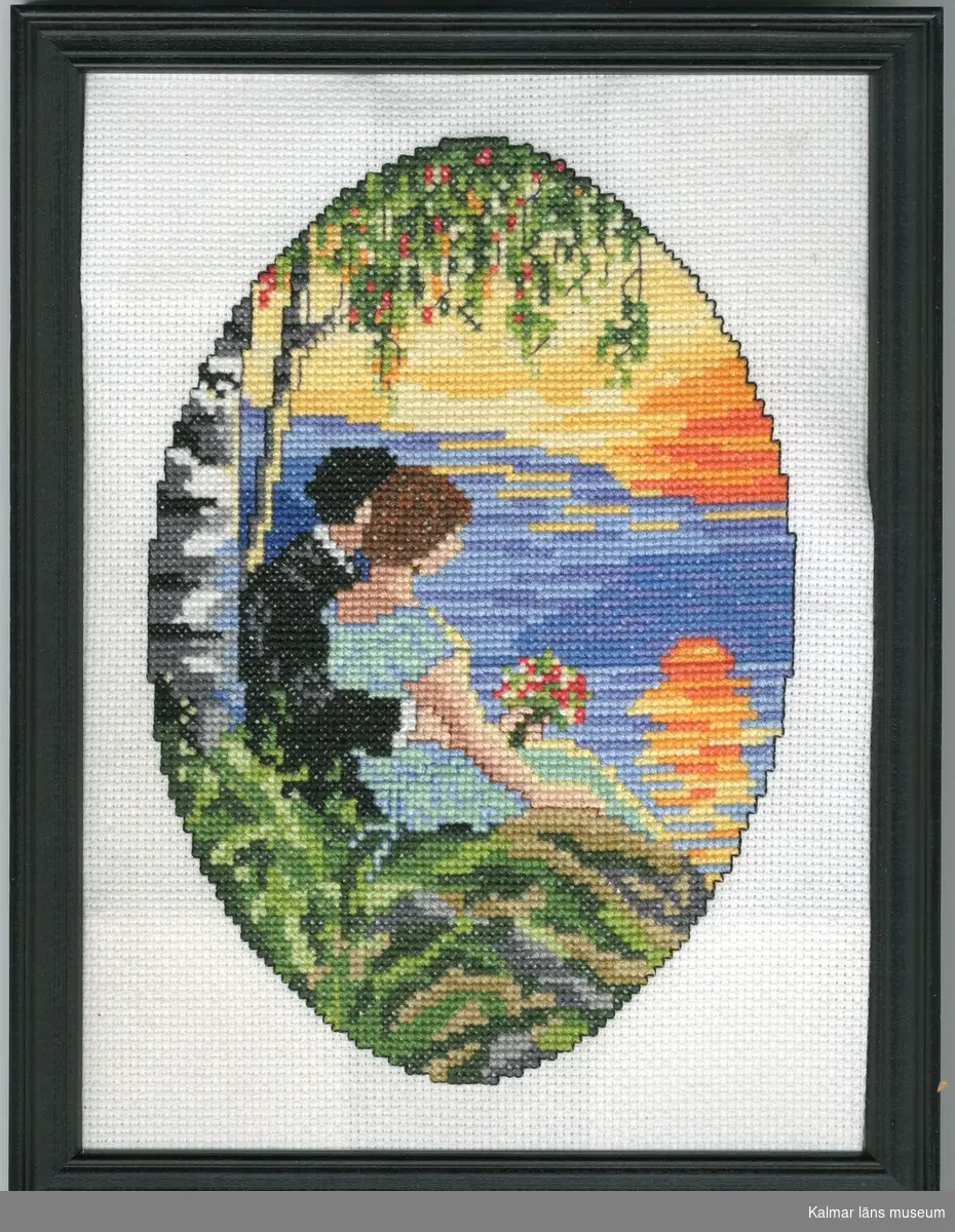 En ung man klädd i svart kostym sitter med armen runt en brunhårig kvinna med blå kortärmad klänning. Hon bär en bukett blommor i handen. De sitter på en sten framför en sjö och tittar ut på en solnedgång eller soluppgång. Bakom dem växer en björk.