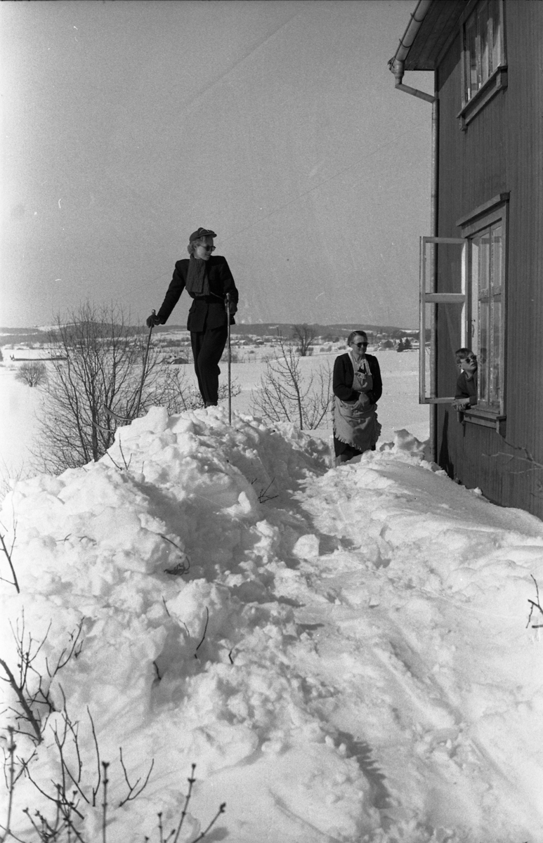 To bilder fra fotografens eiendom Odberg på Kraby mars/april 1951.
På bilde nr. 1 Sigrun Røisli på ski, bror Kjell som sitter på sparken med forstuet ankel, og mor Karine som med nød og neppe finner postkassa inne i snøhaugen.
På bilde nr. 2 Sigrun Røisli og mor Karine på baksida av huset, mens Kjell kikker ut av vinduet.