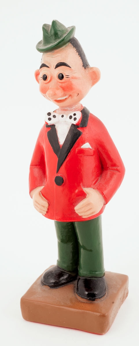 En figur av en mann med grønn hatt og rød jakke som smiler, og holder i jakkelommene sine.