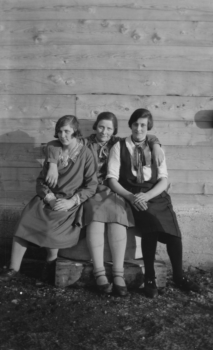 Tre kvinner sittende foran husvegg