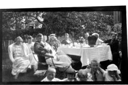 Voksne og barn samlet til teselskap rundt bord i hage i Engl