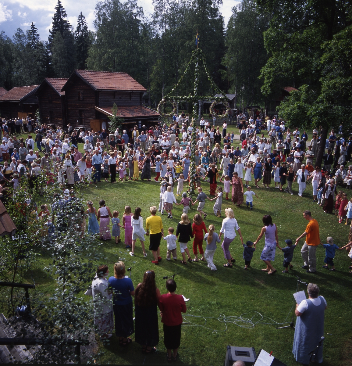 Midsommarfest vid Västerby hembygdsby i Rengsjö år 2000. Solen lyser och stora och små dansar runt midsommarstången.