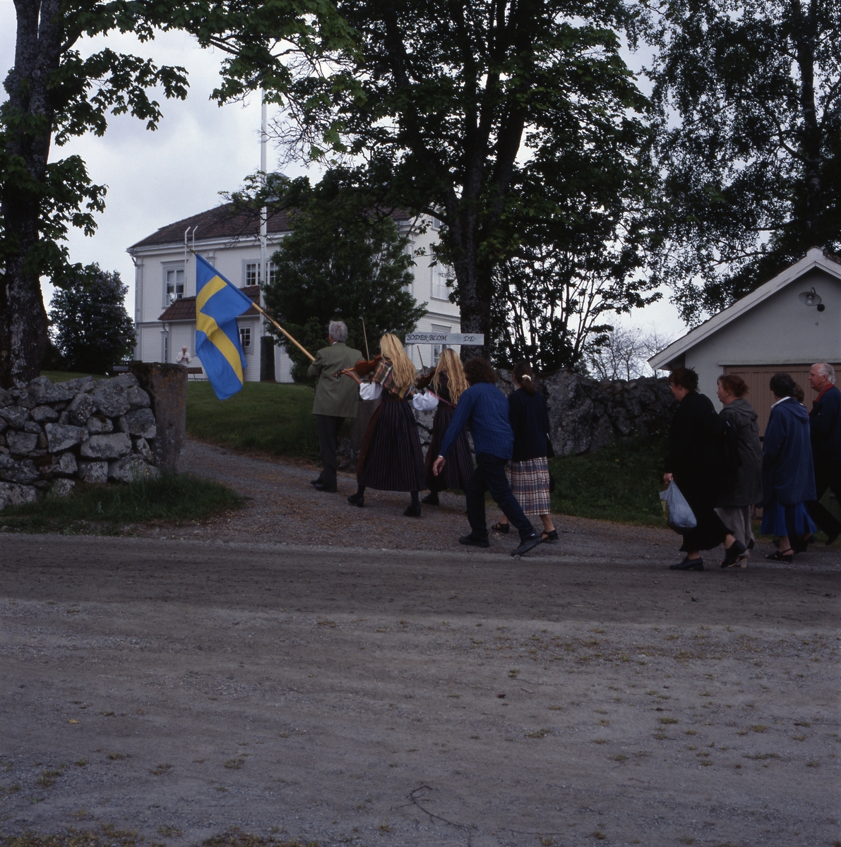 Kyrkvandring i Trönö, söndagen 17 juni 2001. Främst i ledet går en man med fana och efter honom går "Spelsystrarna" med sina fioler. Därefter går resten av deltagarna. Här är de på väg upp mot Söderblomsgården.