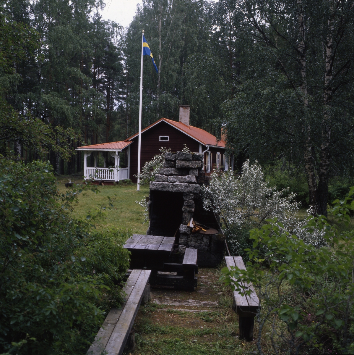 Författaren Albert Vikstens torp vid Ängratörn. Flaggan är hissad och utespisen tänd och omgiven av blommande fruktträd. Ängratörn-veckan med Daisy och Gunnar 10-15 juli 2000.