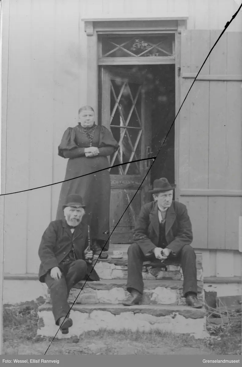 På prestegårdstrappa i Grense Jakobselv, våren 1896. Lærer og kirkesanger Anders Nilsen Tokle og sokneprest Emil Stang Lund sitter på trappa. Fru Kristofa Tokle står bak.