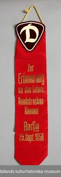 Röd vimpel av konstsiden med guldtext: "Zur Erinnerung an das intern. Rundstrecken-Rennen Berlin 25. Sept. 1956".