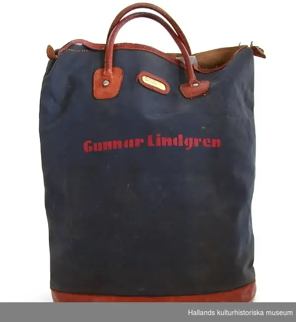 Väska av mörkblå smärting med bruna läderdetaljer. Två bärhandtag samt dragkedja. Tryckt "Gunnar Lindgren" i rött.