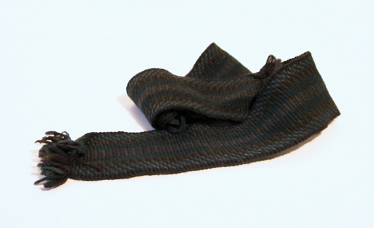 Pinnband, svart, grönt och blågrått, vävt med pinnar. Kallas även "vilkat" eller "plockat" band. Två band vävs samtidigt och vävs ihop på mitten. Band med denna bredd användes till manshalsdukar, smalare till strumpeband.