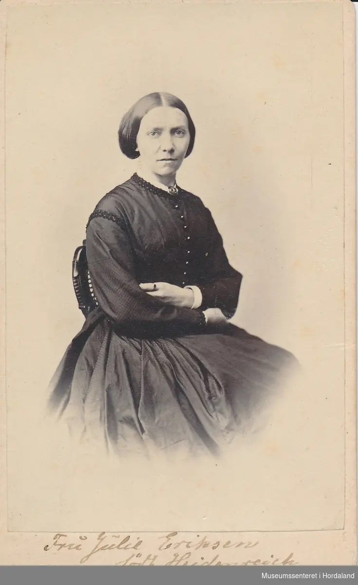 portrettfotografi av kvinne med midtskill og håret samla i nakken, vid svart, langerma kjole med små knappar framme