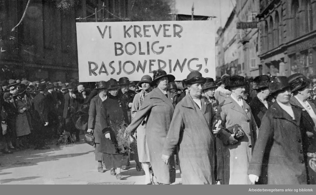1. mai 1925, Arbeiderpartiets kvinneforeninger i Oslo. Demonstrasjonstoget svinger inn på Karl Johans gate fra Universitetsgata. Parole: Vi krever boligrasjonering!..
