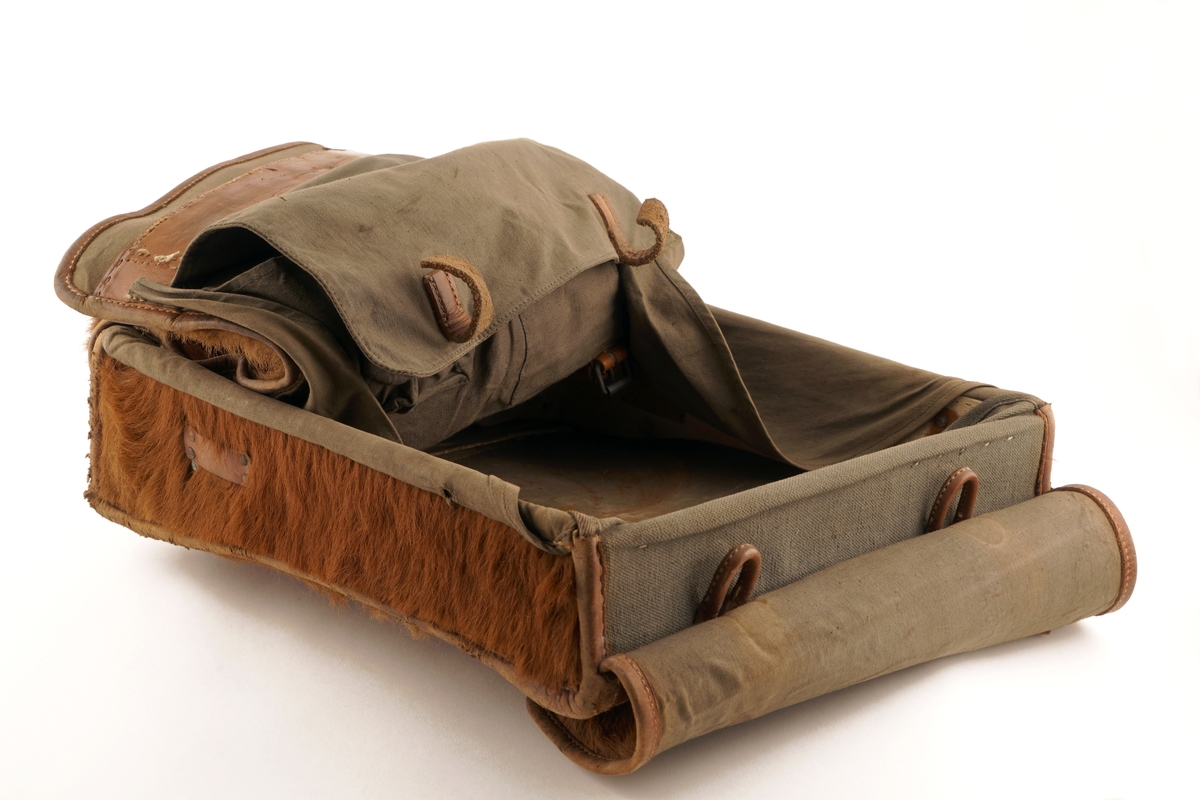 Skinnveske (taske) til å bære på ryggen. Rektangulær med lokk og to spenner for låsing.