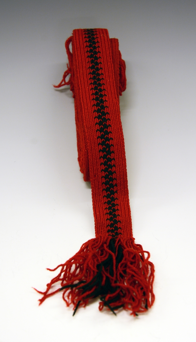 Drakten består av stakk, forkle, 2 trøyer, 2 brikkevevde belter.
C) Brikkevevet band - hårband. Rødt og sort. Fra protokoll.