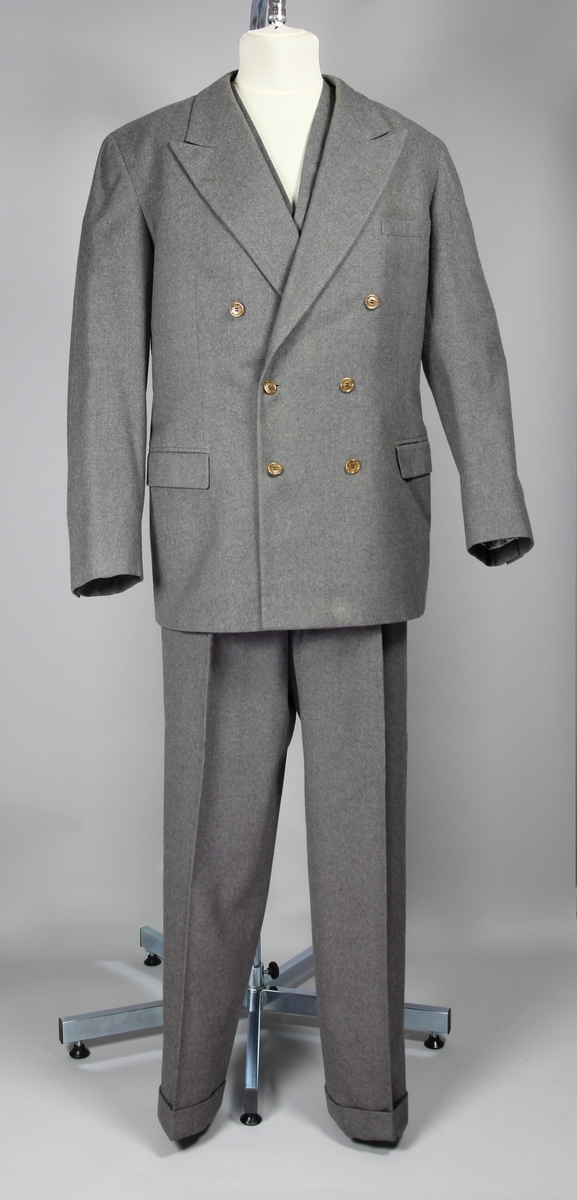 Tredelad kostym i grå yllegabardin. Innehåller dubbelknäppt kavaj, väst och två par byxor.