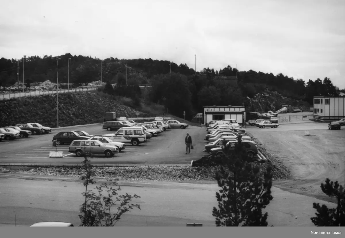 Pressefoto fra parkeringsplassen ved Kvernberget lufthavn på Nordlandet i Kristiansund. Bildet kan trolig dateres mellom 1987-1990. Fotoarkivet stammer fra Nordmørsposten, og inngår nå i Nordmøre museums fotosamlinger.