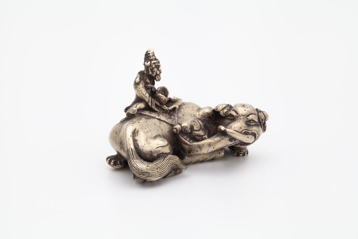 Skulpturen forestiller en mannsfigur som sitters skrevs over ryggen på en liggende elefant. Han er ikledd romslige gevanter og en hatt. Han sitter på et klede med meanderbord og holder i en lotus med begge hendene. Elefanten er dekorert med 6 stjerner.