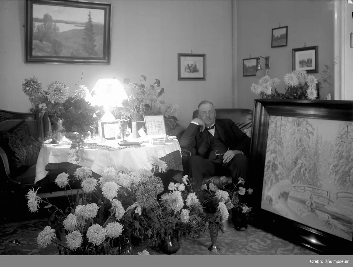 Man med blomsteruppsatser.
Gottfrid Thermaenius på 50-årsdagen 5 november 1921. Tavlan närmast till vänster om Gottfrid är en inramad duk med texten: "Till Pappa på 50 årsdagen av Bengt". Bengt var hans yngste son, som skulle fylla sju år på julafton 1921.