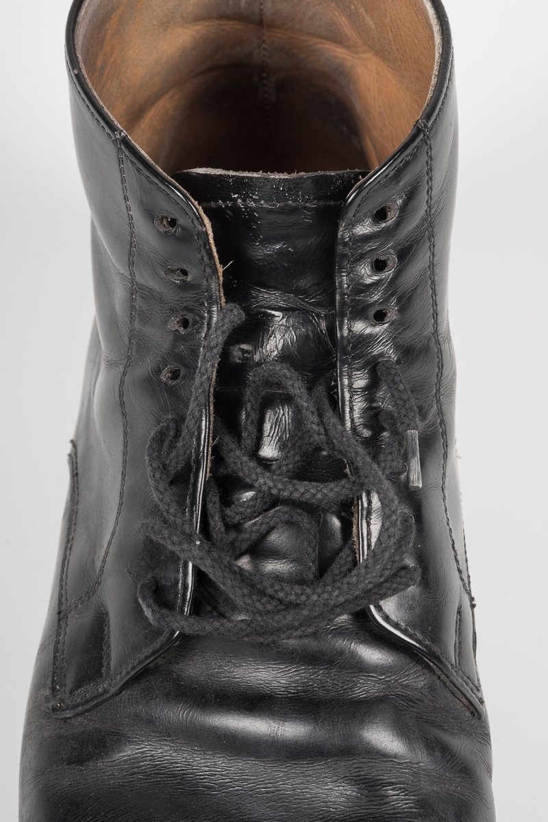 Høyre sko av et par svarte skinnsko med skolisser i bomull.