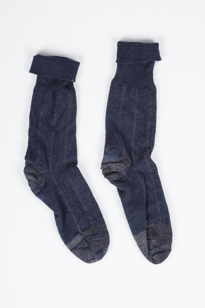 Mørkeblå høye sokker, med grå detaljer og røde og hvite striper. Sokkene er meget godt brukte og stoppet flere ganger. På innsiden øverst er det sydd inn en lapp med fangenummeret 8416, som identifiserer sokkene som Erich Mønnichen Plahtes.