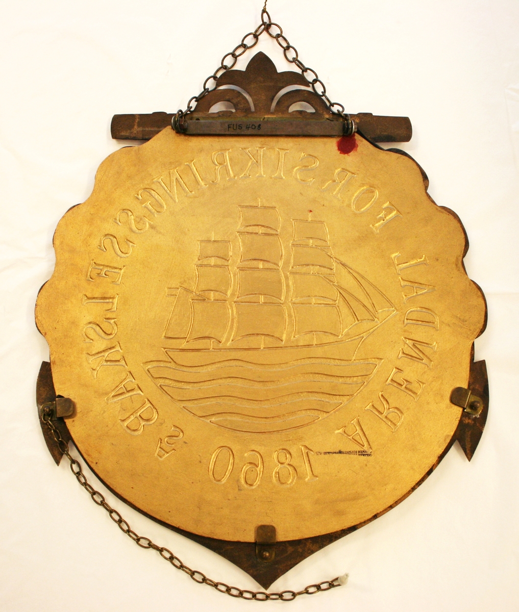 Skiltet har rød bakgrunn, og viser en sort fullrigger med hvite segl, som segler på blått hav. Rundt skipet står det: "Arendal forsikringsselskab AS 1860" i gullfarvede bokstaver.