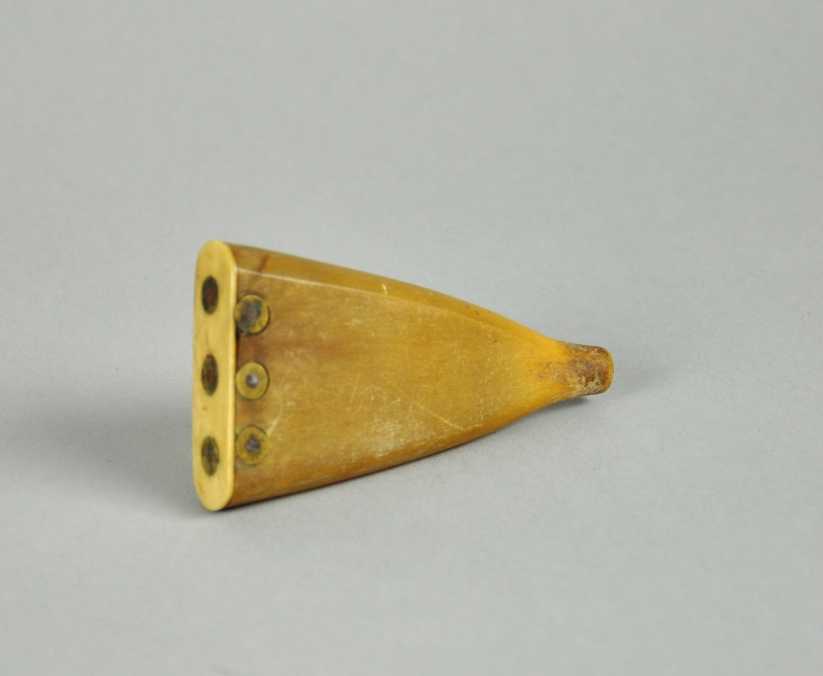 Flat, trekantet snusdåse av kuhorn. Lokk er festet med metallnagler. Det er åpning nederst.