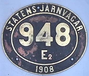 Oval skylt av mässing med text i relief mot svart botten.
Från ångloket SJ E 948, omlittererad 1940 till E2 948.
NOHAB Nº 894.