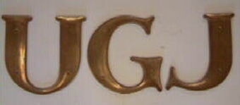 Vagnsemblem bestående av tre stycken mässingsbokstäver som bildar ordet "UGJ".