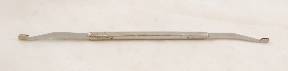 Fjäderbockare av metall med ett handtag i mitten och likadana spegelvända verktyg nitade i skåror i ändarna av handtaget. Verktygen är märkta "0,5".