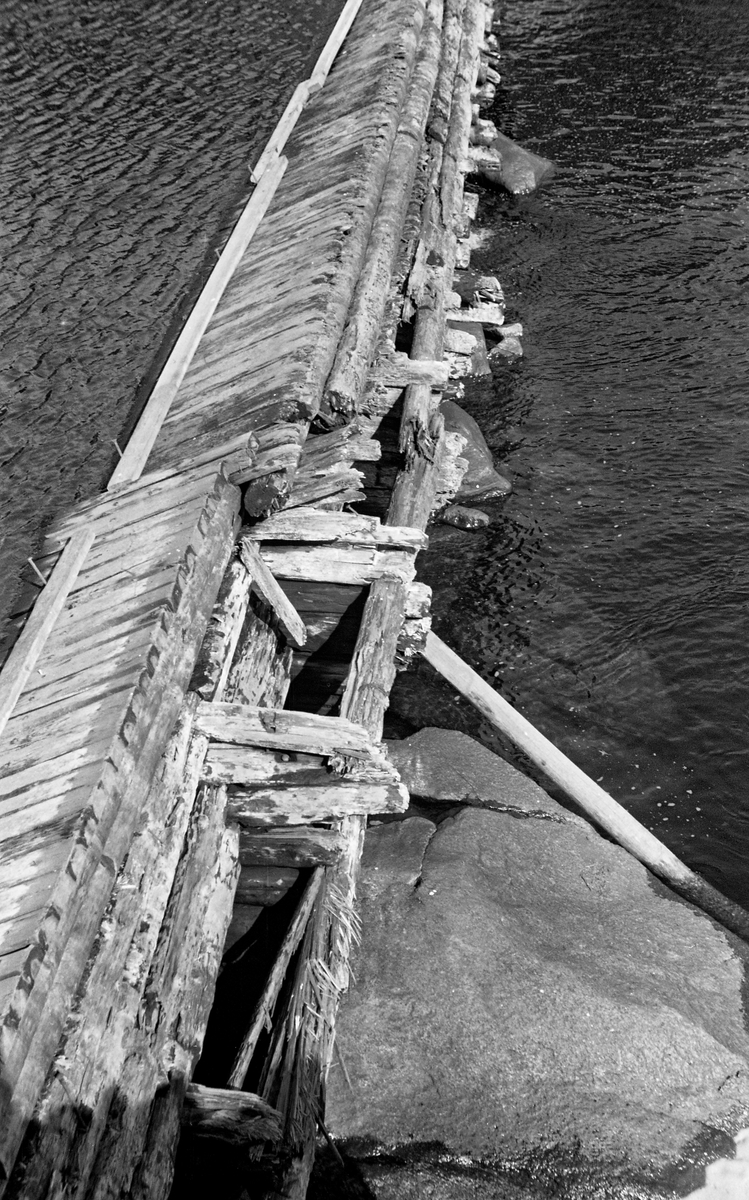 Syversætredammen i elva Flisa i Åsnes i Solør, fotografert fra nordvestre elvebredd i 1955.  Fotografiet er tatt i en tørkeperiode midt på sommeren, da vannføringa i elva var minimal, slik at damkonstruksjonen var godt synlig, uten overløpende vann.  Dermed ble forfallet og råteskadene på tømmerkonstruksjonen tydelige.  Den var åpenbart moden for fornyelse.  Dette fotografiet er tatt skrått ovenfra, ned mot damkrona.  På motstrøms side hadde den plankekledning, lagt som et skråplan for at tømmerstokker og andre legemer som kom flytende med strømmen ikke skulle hekte seg fast, men skyves over.  Plankekledningen kan se ut til å ha vært av noe nyere dato enn den underliggende tømmerkonstruksjonen.  Syversætredammen var en terskeldam som var bygd øverst i fossen, åpenbart for å skape et vannreservoar for det nedenforliggende kvernbruket, muligens også for å heve vannspeilet og lette tømmerfløtinga i det ovenforliggende elveløpet.  Dammen skapte et fall på cirka to meter.  SJF.1989-02316 viser den samme dammen mens den ennå var i god stand og på et tidspunkt da det var mye vann i Flisa.