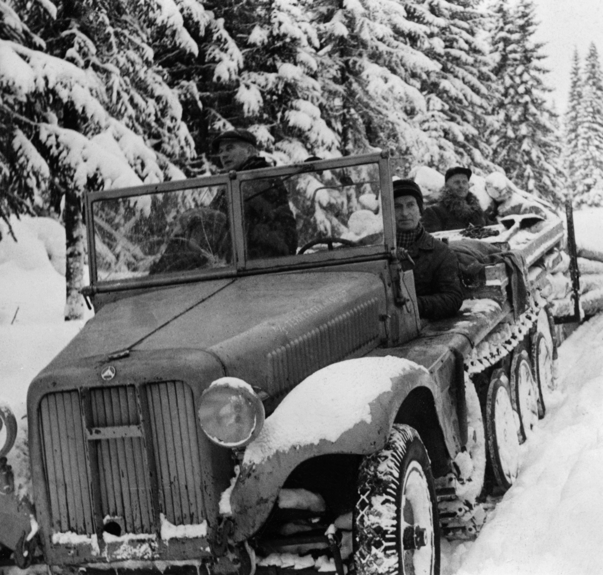 Beltebil som ble brukt i firmaet And. H. Kiær & Co. Ltds forsøk med bruk av motorkjøretøy til tømmertransport i første halvdel av 1950-åra.  Fotografiet er tatt mot fronten av kjøretøyet.  Den ser ut som en lastebil, med motorkasse, skjermer, lykter og gummihjul på forstillingen, som på en vanlig lastebil.  Bakparten av kjøretøyet gikk på belter.  Bilen hadde ikke overbygde førerplasser, men ei todelt frontrute.  Bak denne ser vi to karer.  Bakenfor skimtes den spesialbygde rustningen, en todelt tømmerslede med kraftige stålstaker på sidene.  På denne sleden sitter skogsbestyrer Ole P. Sandbæk.  Vi er usikre på identiteten til e to karene som sitter på kjøretøyet.  Jørgen Salberg og Semming Andreassen var imidlertid også med på forsøksdriftene med motorisert tømmertransport i Stor-Elvdal.  Fagbladet «Skogeieren» hadde i 1950 en reportasje der de fulgte ei tømmervending hvor det ble transportert 80 stokker med et slikt kjøretøy, som i motsetning til tilsvarende doninger for hest, hadde kraftige stålstaker på sidene og et eget ståldrag i fronten.  I tillegg til det tømmeret som befant seg på sleden, var det altså vanlig at kjørerne la «etterslått», en serie av tømmerfloer som ble slept på den snøpakkete vegen bak beltekjøretøyet og rustningen.  Det lasset fagbladet «Skogeieren» fulgte besto til sammen av 145 stokker og hadde et volum på 18,7 kubikkmeter.  Denne transportmåten skal ikke ha vært like hemmet av snøfall eller mildvær med klabbeføre som sledekjøring med hest.  Forstmannen Hans Berger, som var skogsbestyrer hos And. H. Kiær & Co. Ltd. og hadde ansvaret for en del av beltebildriftene, rapporterte om at de både gjorde det mulig å hente tømmer fra steder som var langt på veg utilgjengelige med hest, og at driftskostnadene per kubikkmeter ble noe lavere med motorisert transport (jfr. notat som er gjengitt under fanen «Opplysninger»).

Gunnar Garen har i en kommentar til presentasjonen av dette motivet på nettstedet «DigitaltMuseum» (2. mai 2015) skrevet følgende:

«Dette er en kanontrekkvogn fra ca. 1940, trolig en 3 tonner fra Sveitsiske Saurer, men mange lagde disse.  Kunne trekke en kanon på 3 tonn.  Største kunne trekke 12 tonns kanon.»

Seinere har vi mottatt følgende spesifikasjon:

"Sveitsisk Saurer halvbelter, Sd.Kfz. 10 - Sonder-Kraftfahzeuge 10 (løpenummer) fra 2. verdenskrig, produsert av ulike fabrikker for tyske Wehrmacht. Også kalt Zugkraftwagen 1 t - lettere trekkvogn for 1-tonns trekkraft i terreng."

Høsten 2020 kom følgene kommentar fra Asbjørm Rolseth:

«Ikke bland Sveits inn i dette. Sveits var et nøytralt land under 2. verdenskrig og produserte aldri krigsmateriell for tyske Wehrmacht. Moderfirmaet Saurer i Sveits var medeier i Österreichische Saurer-Werke AG, etablert i 1914, men solgte seg ut i 1937. Saurer i Østerrike fortsatte som eget firma og ble involvert i tysk krigsproduksjon etter at Østerrike ble tilsluttet Tyskland i 1938. Saurer i Østerrike var en av seks produsenter av denne typen halvbeltebil. Bilen på bildet kan like godt være produsert av en av de andre.»

Mer informasjon om And. H. Kiær & Co's bruk av beltebilen finnes, som nevnt, under fanen «Opplysninger».