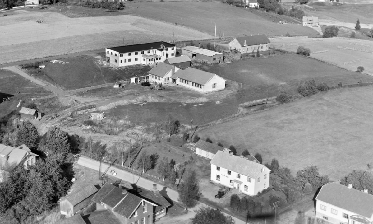 Svart-hvit foto tatt fra luften av hus med jorder rundt.