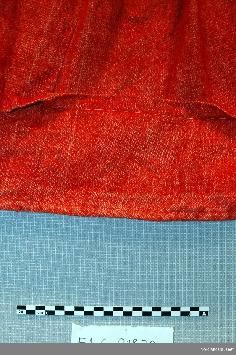 Rødt ullskjørt med splitt i siden. Stoffet er lerretsvevd i rødt og hvitt. Linningen er ikke foldet forran, foldet på sidene og rynket helt bakerst.  lukkes med hempe i metall. 

Hvitt kantebånd av ull i linningen. Skjørtet er sydd på maskin. 

Nederst på skjørtet er det sydd en pyntefold. Denne er sydd opp for hånd med lange (tråkle aktige) sting.