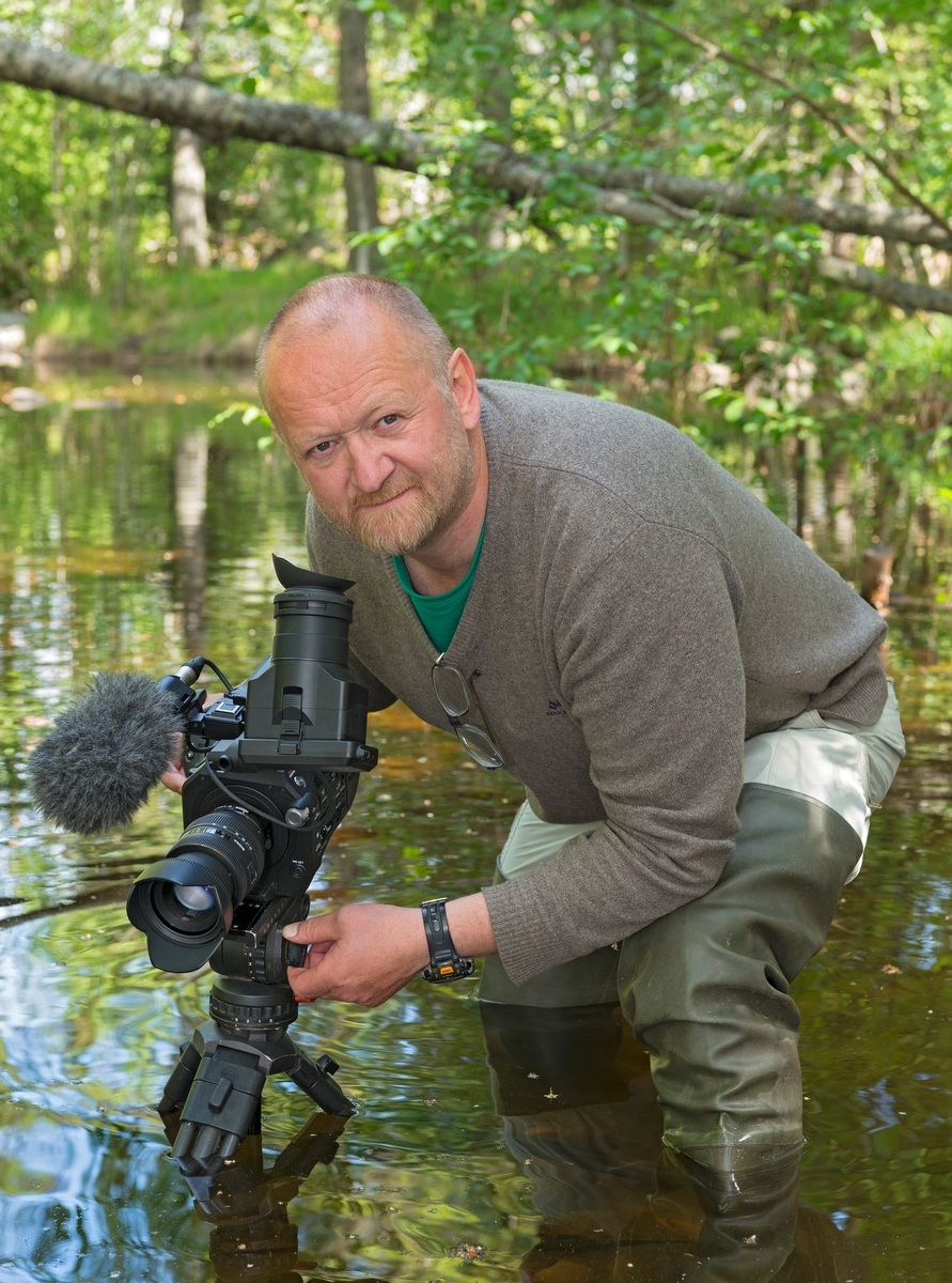 Filmfotograf Geir Bernhard Randby, fotografert med stativmontert kamera i vann.  Fotografiet er tatt i Norsk Skogmuseums friluftsmuseum på Prestøya i Glomma i Elverum, der Randby håpte å få opptak av bekkeniøye (Lampetra planeri) til NRK-programserien «Ut i naturen».